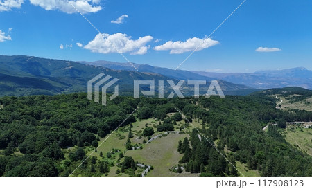 Breathtaking view of lush green valleys and distant mountains under a blue sky with fluffy clouds 117908123