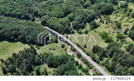 Aerial view of a historic railway viaduct nestled among lush green forests and rolling hills on a sunny afternoon Aerial view of a historic railway viaduct nestled among lush green forests and rolling hills on a sunny afternoon 117908124