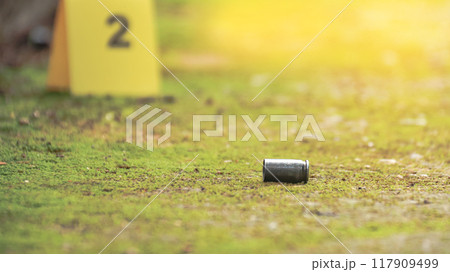 Spent bullet casing lying on the ground with blur number 2 sign. Concepts of shooting sports and security highlighting the dual nature of firearms in both competitive sport and protective measures. Spent bullet casing lying on the ground with blur number 2 sign. Concepts of shooting sports and security highlighting the dual nature of firearms in both competitive sport and protective measures. 117909499