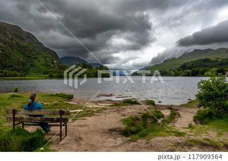 Woman On Bench Looking Over Lake Loch Shiel At Glenfinnan Monument On The Road To The Isles In Lochaber In Scotland, UK Woman On Bench Looking Over Lake Loch Shiel At Glenfinnan Monument On The Road To The Isles In Lochaber In Scotland, UK 117909564