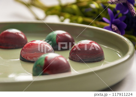 Collectible handmade tempered chocolate candies with a glossy painted body on a round plate with a blurred background and bokeh elements Collectible handmade tempered chocolate candies with a glossy painted body on a round plate with a blurred background and bokeh elements 117911224