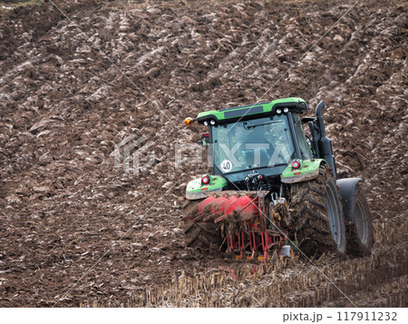 Farm tractor furrowing arable field 117911232