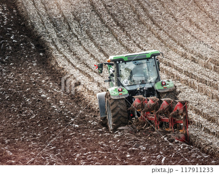 Farm tractor furrowing arable field 117911233