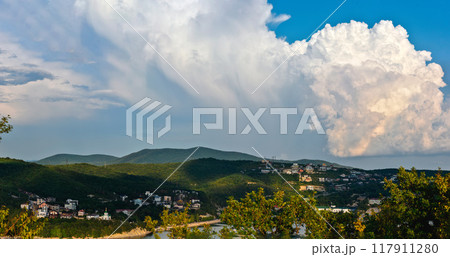 The breathtaking view of stunning cloud formations hanging gracefully above a peaceful hillside community 117911280