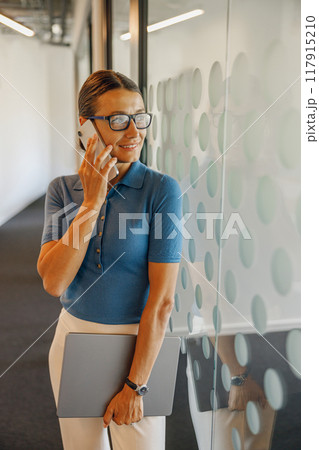 A professional woman is conversing on her phone in a sleek, modern office environment A professional woman is conversing on her phone in a sleek, modern office environment 117915210