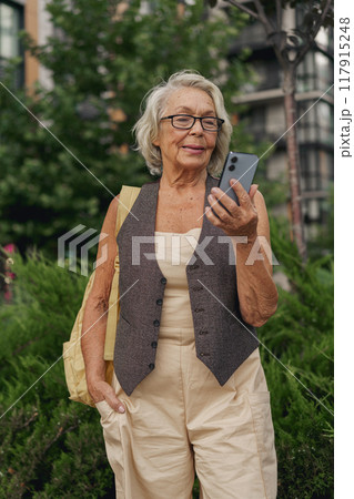 An Elderly Woman Actively Engaged with Her Smartphone in a Vibrant Urban Park Setting An Elderly Woman Actively Engaged with Her Smartphone in a Vibrant Urban Park Setting 117915248