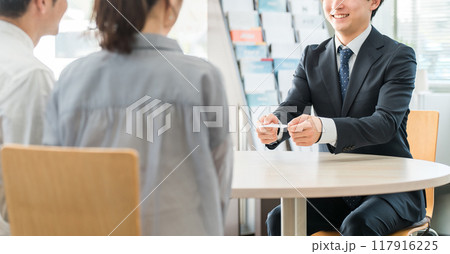 ショールーム・商談スペースで名刺を渡す若いアジア人ビジネスマンと客の夫婦 117916225