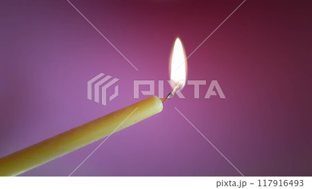 Burning candle on a pink background. A fragile, thin candle on a beautiful pink background. Burning candle on a pink background. A fragile, thin candle on a beautiful pink background. 117916493