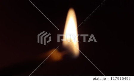 Burning candle in the dark, out of focus. The edge of the candle is slightly visible near the flame, and the flickering of the fire appears to me as a slight blur. 117916495