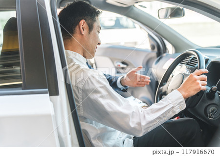 ショールームで自動車の車内で営業マンの説明を受ける顧客の男性 ショールームで自動車の車内で営業マンの説明を受ける顧客の男性 117916670