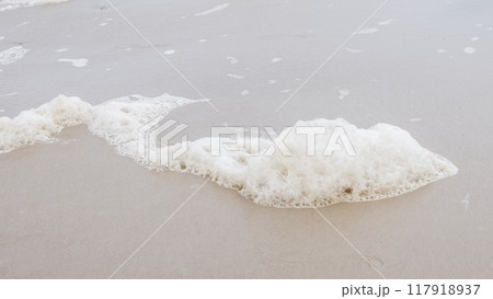 Delicate White Sea Foam on Sandy Beach with Gentle Waves in Background 117918937