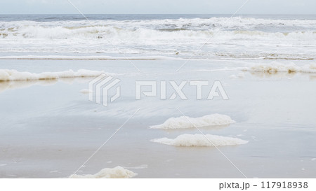 Delicate White Sea Foam on Sandy Beach with Gentle Waves in Background 117918938
