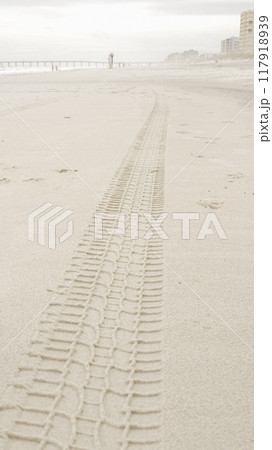 Close-up view of a detailed tire track left by a large vehicle on a sandy beach. 117918939