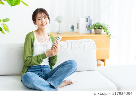部屋でスマホを操作する若い女性 117924394