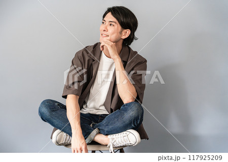 椅子に座るスニーカーとジーンズ姿のさわやかな男性 117925209
