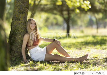 Young woman relaxing under tree in a park Young woman relaxing under tree in a park 117925893