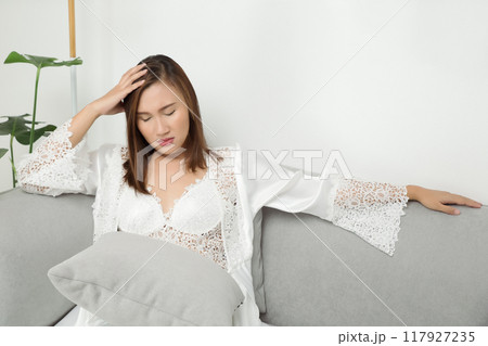 A woman in a white nightgown appears distressed by a headache during the night. A woman in a white nightgown appears distressed by a headache during the night. 117927235