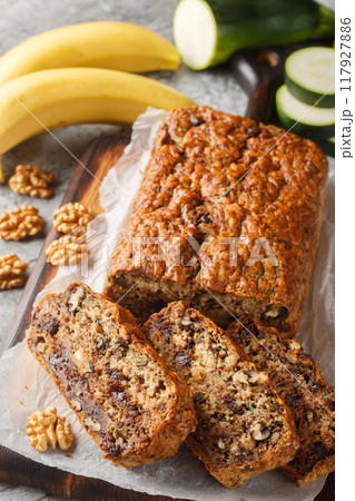 Loaf of dessert zucchini banana bread with walnuts and dark chocolate close-up on wooden board. Vertical 117927886