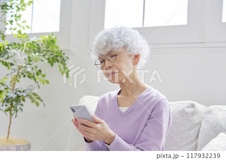 スマートフォンを使いながら悩むシニア女性　リビングルーム 117932239