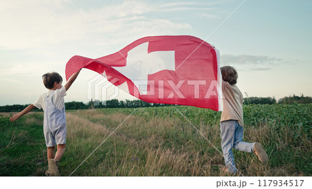 Swiss little kids patriot children runs with national flag on nature background. Celebration banner Swiss little kids patriot children runs with national flag on nature background. Celebration banner 117934517