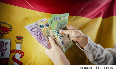 Spanish flag background. Woman counting money euros. Credits, raising tariffs in EU Europe 117934559