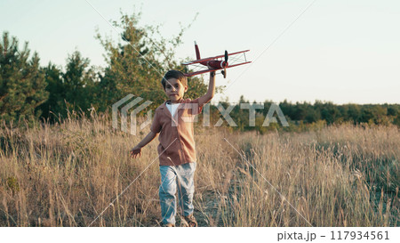 Smiling 5 years old child boy running with wooden vintage airplane. Kid dreaming to be pilot 117934561