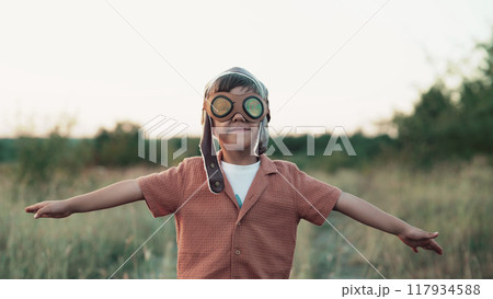 Portrait of funny little boy in aviator helmet wearing protective eyeglasses and ready to fly as 117934588