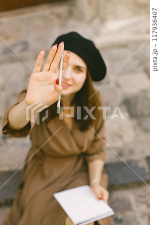 Portrait of a female painter painting while sitting in a city center. A woman wearing khaki dress and a black hat. Girl posing for a photo. Portrait of a female painter painting while sitting in a city center. A woman wearing khaki dress and a black hat. Girl posing for a photo. 117936407
