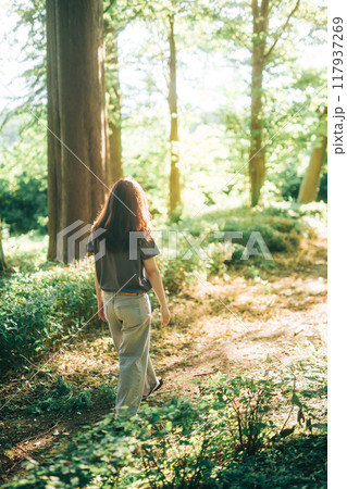 木漏れ日の夕日の光が差し込む森の中を散策する女性 117937269
