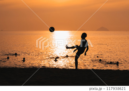 Silhouette of a man kicking a ball playing traditional Asian beach soccer on beach by the sea at sunset Silhouette of a man kicking a ball playing traditional Asian beach soccer on beach by the sea at sunset 117938621