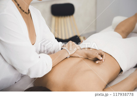 Process of back massage in pro salon. Hands of female therapist on a body of a woman laying face down on massage table, close-up, selective focus. 117938778