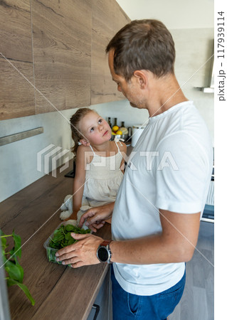 Family with a young father and his little daughter preparing greens for a healthy juice or smoothie in home kitchen 117939114