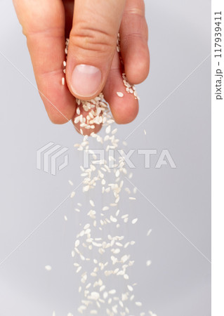 Hand pouring white sesame seeds on gray background Hand pouring white sesame seeds on gray background 117939411