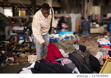 Man in an African suit chooses second-hand clothes at a flea market in 117939940