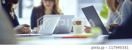 Close-up of a coffee cup on a table with laptops during a business meeting. Casual teamwork and collaboration in a modern office. 117940381
