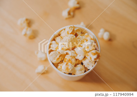 A bucket of popcorn, top-view, warm colors, light brown wooden background, flat lay, daylight macro close-up 117940994