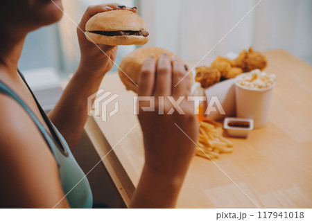 Binge eating disorder concept with woman eating fast food burger, fired chicken , donuts and desserts Binge eating disorder concept with woman eating fast food burger, fired chicken , donuts and desserts 117941018