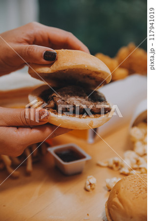 fast food, people and unhealthy eating concept - close up of woman hands holding hamburger or cheeseburger 117941019