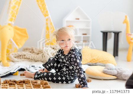 Little girl in pajamas plays with letters carved out of wood in her nursery 117941373