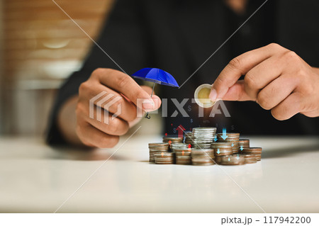 Businessman holding a small red umbrella over a stack of coins. Concept of financial protection and security Businessman holding a small red umbrella over a stack of coins. Concept of financial protection and security 117942200
