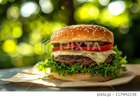 Juicy cheeseburger with lettuce, tomato, pickles, and sesame bun in natural daylight bokeh background 117942236