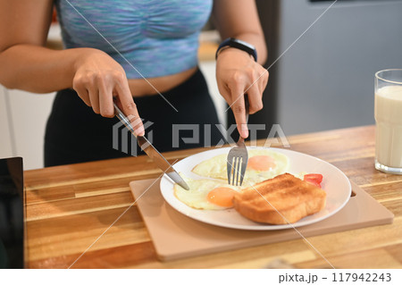 Close up image of a woman enjoying breakfast on the wooden countertop with a glass of milk for nutritious meal Close up image of a woman enjoying breakfast on the wooden countertop with a glass of milk for nutritious meal 117942243