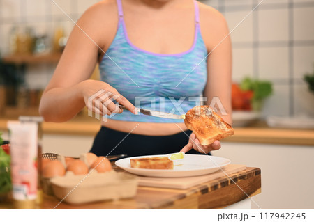 Cropped shot of young woman spreading butter on bread, preparing breakfast in the kitchen 117942245