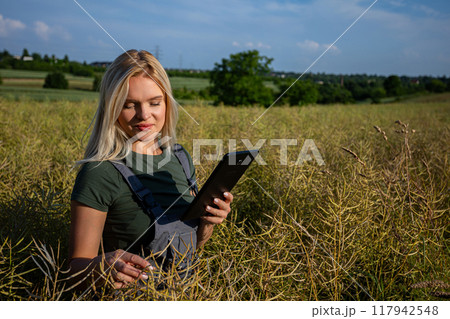 A woman farmer checking the quality of rapeseed on the field and holding a tablet A woman farmer checking the quality of rapeseed on the field and holding a tablet 117942548