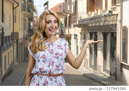 Portrait of happy blonde mature woman advertising copy space. European town street in the background. Portrait of happy blonde mature woman advertising copy space. European town street in the background. 117943380