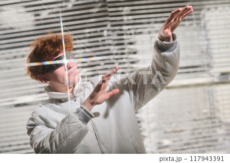 Individual standing against a striped background, raising hand and gazing into sunlight wearing a light-colored jacket. Reflections creating visual effects Individual standing against a striped background, raising hand and gazing into sunlight wearing a light-colored jacket. Reflections creating visual effects 117943391