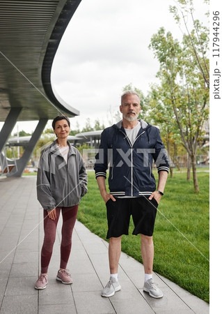 Vertical shot of senior smiling woman and man in sportswear on regular morning workout looking at camera and posing at city park, copy space Vertical shot of senior smiling woman and man in sportswear on regular morning workout looking at camera and posing at city park, copy space 117944296