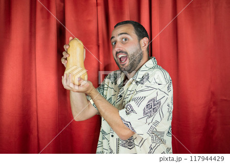 Funny young adult man with white shirt playing with Pumpkin and biting it Funny young adult man with white shirt playing with Pumpkin and biting it 117944429