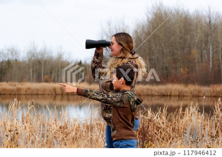 A mom and a son are exploring the nature in the park near the lake. 117946412