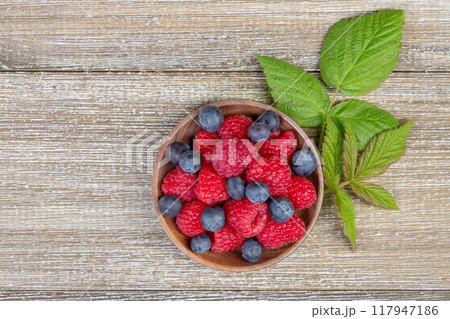 Plate with raspberries and blueberries with leaves on the wooden rustic table. 117947186